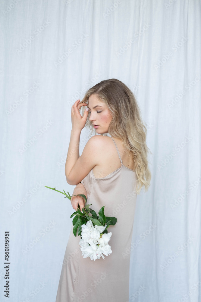 beautiful sensual girl with long blonde hair in dress with a bouquet of pink peonies flowers. Close-up portrait of a woman in studio on a gray white background.concept of feminity spa beautiful sensual girl with long blonde hair in dress with a bouquet of pink peonies flowers. Close-up portrait of a woman in studio on a gray white background.concept of feminity spa