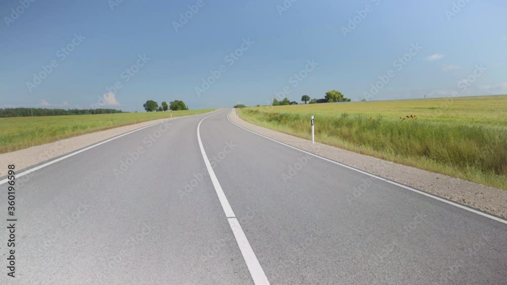 Winding asphalt road in Latvia. Along the edges sown fields of argo with cereals to the horizon. Red poppies on the sidelines. Camera Lift Over Lane. Baltic state Winding asphalt road in Latvia. Along the edges sown fields of argo with cereals to the horizon. Red poppies on the sidelines. Camera Lift Over Lane. Baltic state