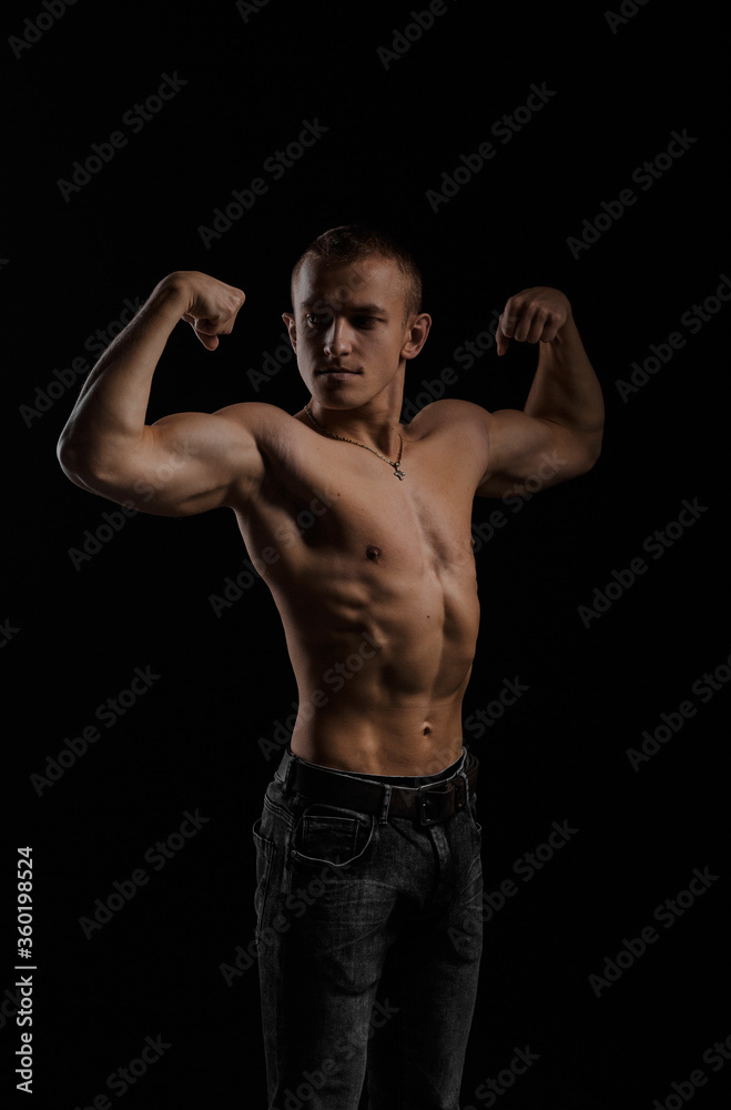 Young attractive bodybuilder with a naked torso poses for the photographer on a black background.