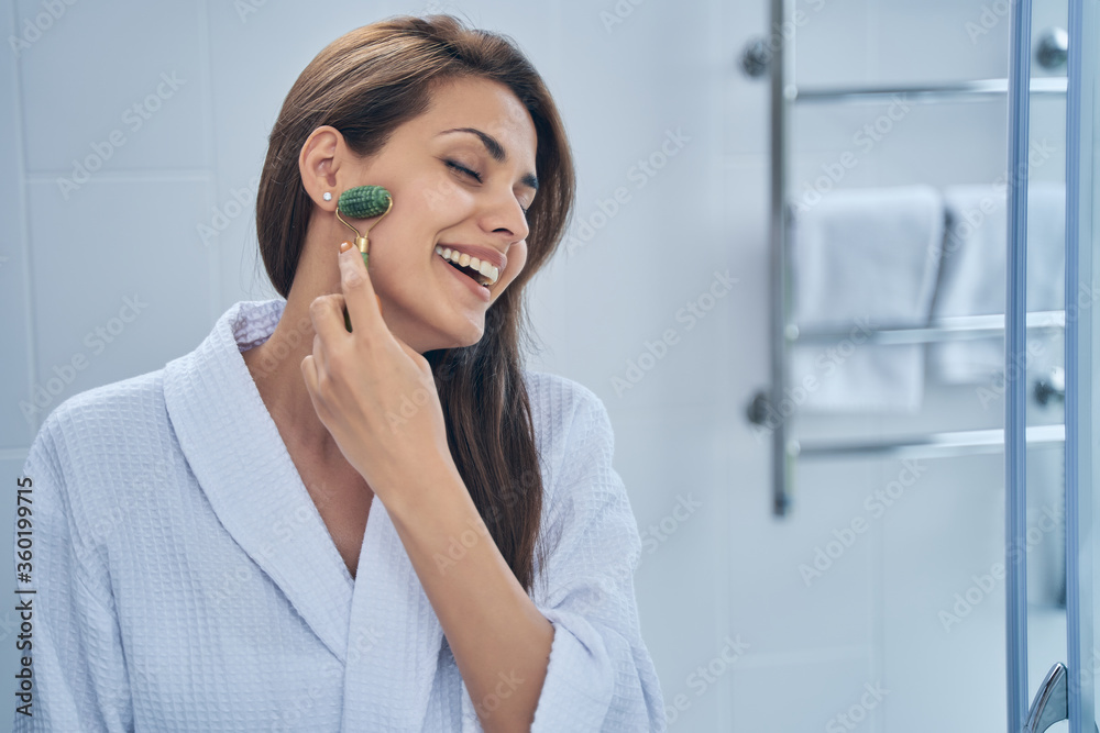 Cheerful young woman using face massager in bathroom Cheerful young woman using face massager in bathroom