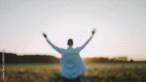 A caucasian man standing on the beautiful field during summer sunset, his hands are raised. A man look at the sky and pray. A man stand with his back to the camera. Defocusing Close up. SLOW MOTION