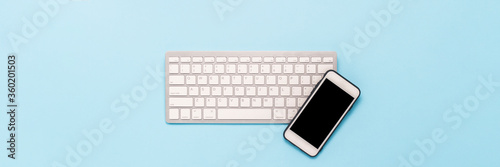Keyboard and white mobile phone on a blue background. Business concept, office work, mobile app and website. Banner. Flat lay, top view.