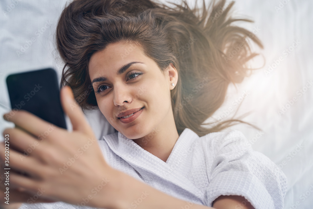 Fototapeta premium Charming young woman lying in bed and making selfie