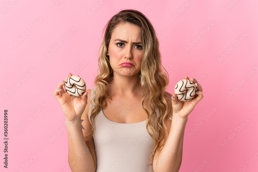 Young Brazilian woman isolated on pink background holding donuts with sad expression
