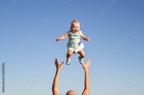 Man throws baby up against the blue sky. Concept game with children, happy family