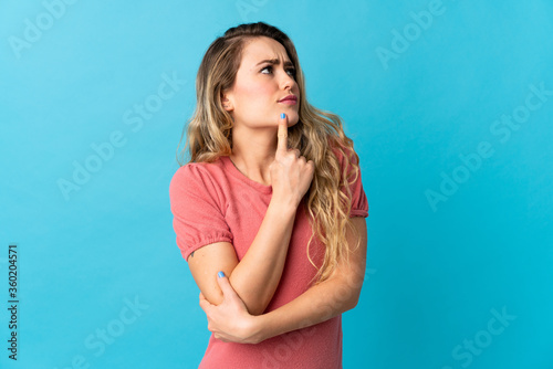 Young Brazilian woman isolated on blue background having doubts while looking up