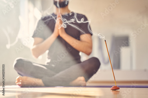 Young man practicing yoga in studio with incense stick photo