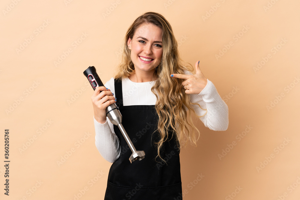 Young brazilian woman using hand blender isolated on beige background giving a thumbs up gesture Young brazilian woman using hand blender isolated on beige background giving a thumbs up gesture