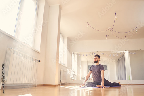 Bearded young man doing pigeon pose in yoga studio