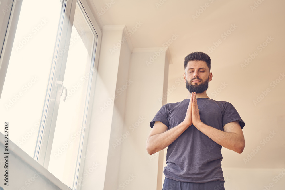 Handsome young man meditating by the window