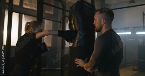 Female boxer hitting a huge punching bag at a boxing studio. Woman boxer practicing with boxing trainer
