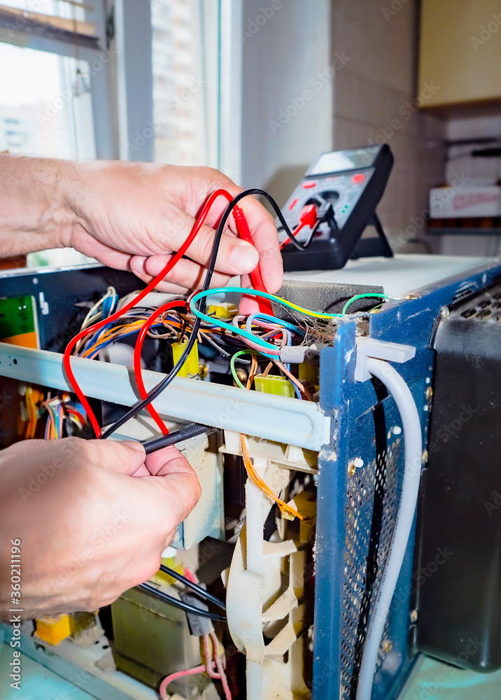 man repairing microwave. Repair of a microwave oven, repair of household appliances. Microwave with side panel removed, internal device visible man repairing microwave. Repair of a microwave oven, repair of household appliances. Microwave with side panel removed, internal device visible