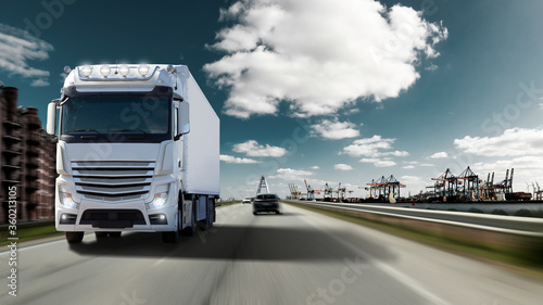 Fast moving truck with full lighting on a motorway with port for container ships. Water, cranes and warehouses with an imposing sky.  © Olaf Simon