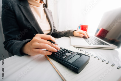 Businesswomen hands working with finances about cost and calculator and laptop with tablet  smartphone at office in morning light