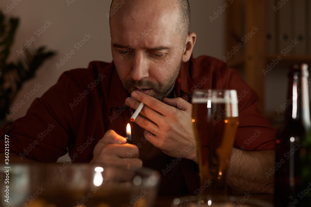 Mature man sitting at the table smoking cigarette and drinking beer