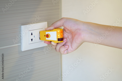 Photo Hand holding electric tester for checking plug at the power outlet in on the wall