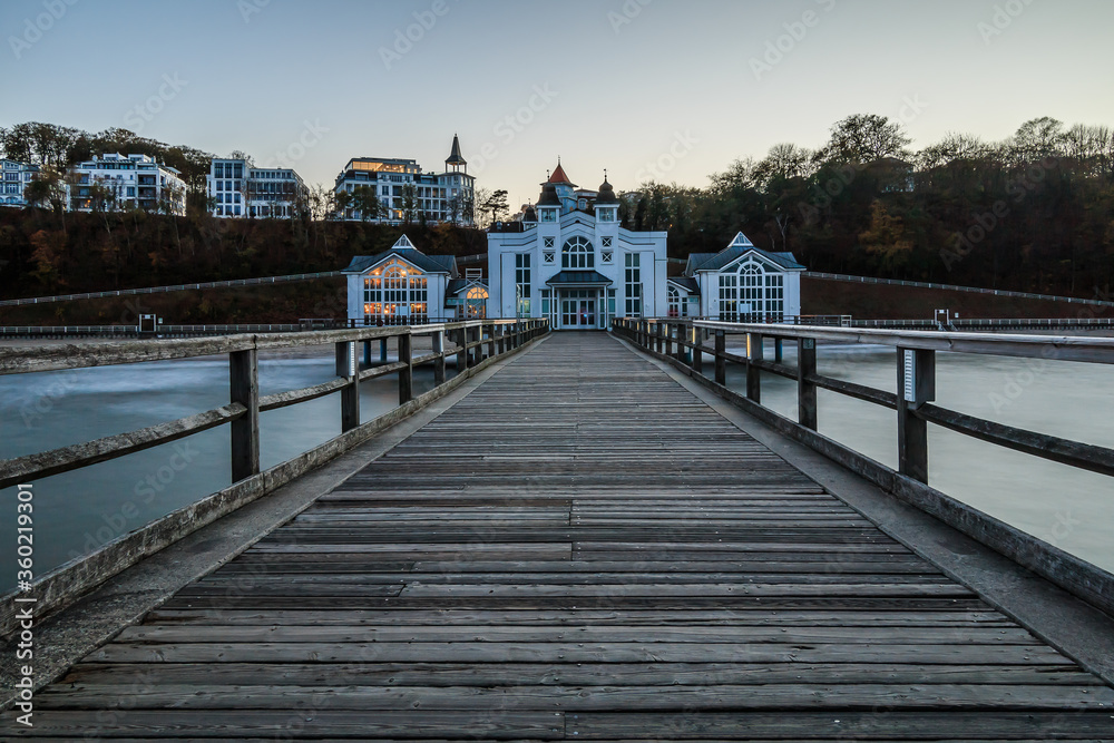Evening mood on the Baltic Sea. Wooden pier with a view of Sellin. Coast section with a jetty without lighting and the buildings on the Baltic Sea coast for autumn at the lido with waves