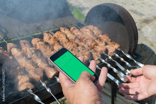 man is frying a barbecue and holding a cell phone. concept of accepting online orders for food preparation.