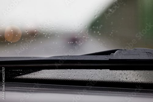 Fragment mokrej od deszczu szyby w samochodzie wraz z wycieraczką, widok z wnętrza auta. Rozmyte tło.