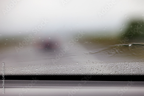Fragment mokrej od deszczu szyby w samochodzie, widok z wnętrza auta. Rozmyte tło.
