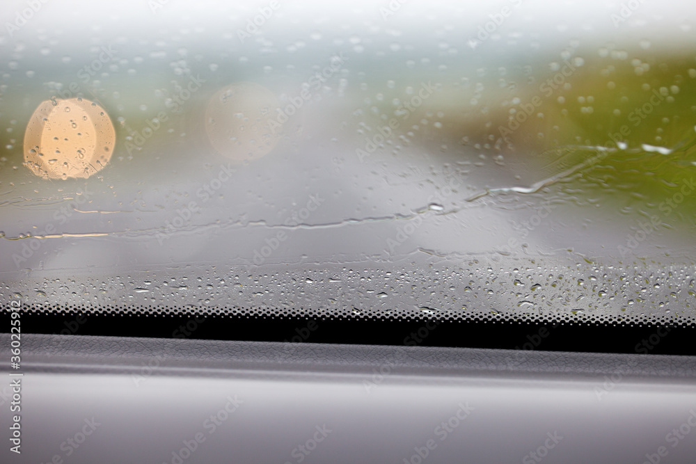 Fragment mokrej od deszczu szyby w samochodzie, widok z wnętrza auta. Rozmyte tło. - obrazy, fototapety, plakaty 