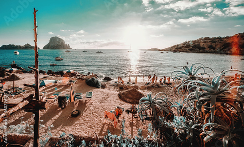 View of Cala d'Hort Beach in Ibiza. Unrecognizable tourists relaxing hanging out on the picturesque famous seaside with Es Vedra rock picturesque view during sunset. Balearic Islands. Espana, Spain