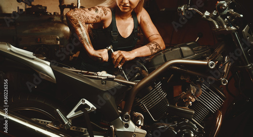 Blond woman mechanic repairing a motorcycle in a workshop