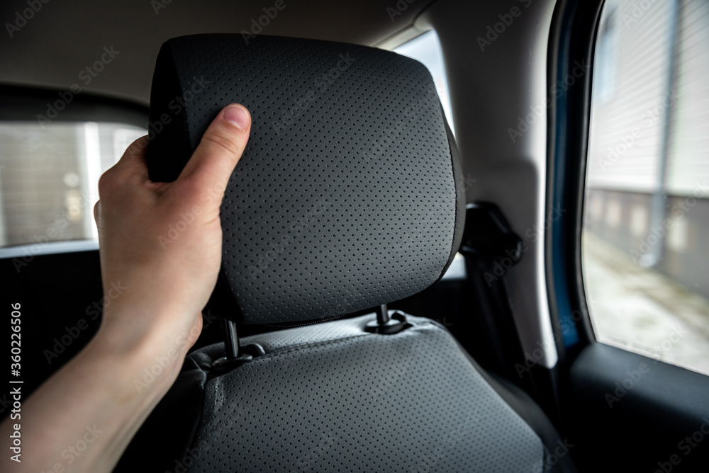 Hand adjusts leather headrest in car interior. Hand adjusts leather headrest in car interior.