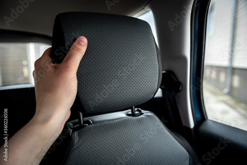 Hand adjusts leather headrest in car interior. © Natallia
