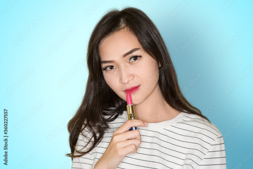 Beautiful Asian young brunette girl with curly hair applying pink lipstick on blue background Beautiful Asian young brunette girl with curly hair applying pink lipstick on blue background