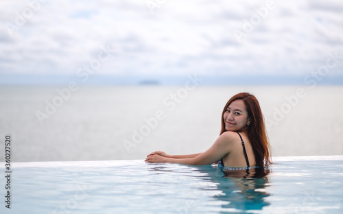 A young asian woman relaxing in infinity swimming pool with a beautiful sea view