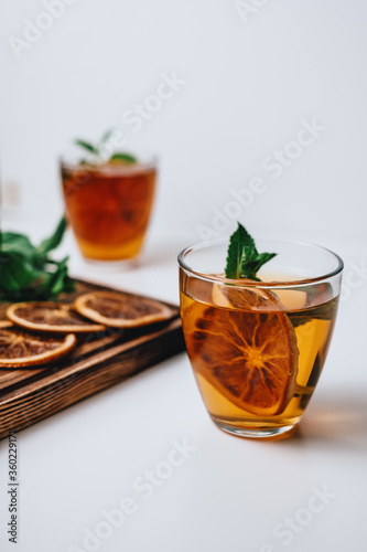 Golden drink, iced tea with a ring of dried orange and mint on a white background.