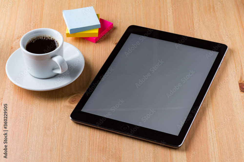 A light wood desktop table with a cup of coffee, a tablet and some colour note paper around A light wood desktop table with a cup of coffee, a tablet and some colour note paper around