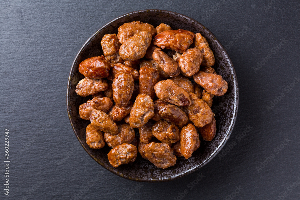 Amêndoas caramelizadas em pote de ceramica sobre pedra de ardósia escura vista de topo Amêndoas caramelizadas em pote de ceramica sobre pedra de ardósia escura vista de topo