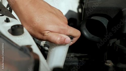 Check the car liquid. Windshield wiper fluid is being poured up to top before mechanic places cap over top of container.