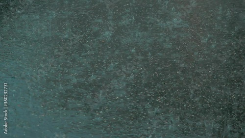 Rain in the city: Raindrops hit the asphalt. Handheld shot. 
Shallow depth of field.