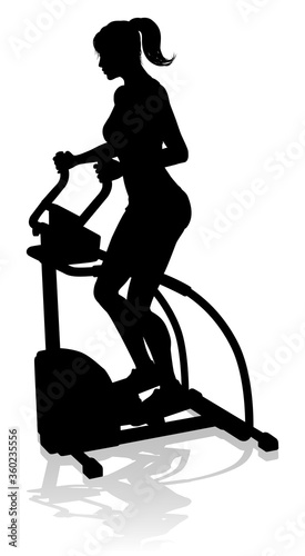 A woman in silhouette using an elliptical cross fit gym equipment exercise machine