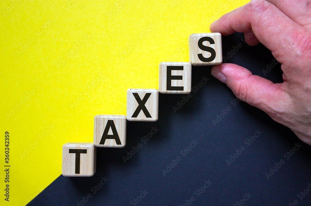 Obraz premium Wood cubes with word 'taxes' stacking as step stair on paper yellow and black background, copy space. Male hand. Business concept success process.