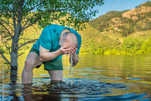 senior, athletic man is splashing and rinsing his face in a mountain lake - summer morning on Horsetooth Reservoir in Colorado