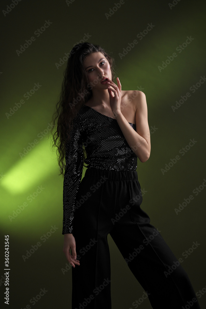 A beautiful young tall girl with long black hair poses in a shiny blouse and black culottes on a green background. Buty and fashion photo shoot. A beautiful young tall girl with long black hair poses in a shiny blouse and black culottes on a green background. Buty and fashion photo shoot.