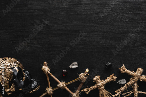 top view of voodoo dolls, ancient crystals, pentagram and skull on black photo