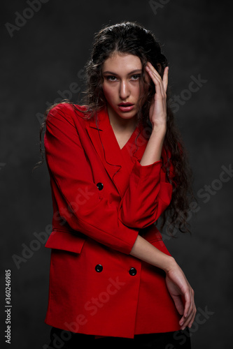A young beautiful oriental woman with long black hair in a red jacket against a black background. The fashion model poses in the studio.