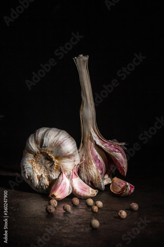 Two heads of garlic and black pepper on a dark background