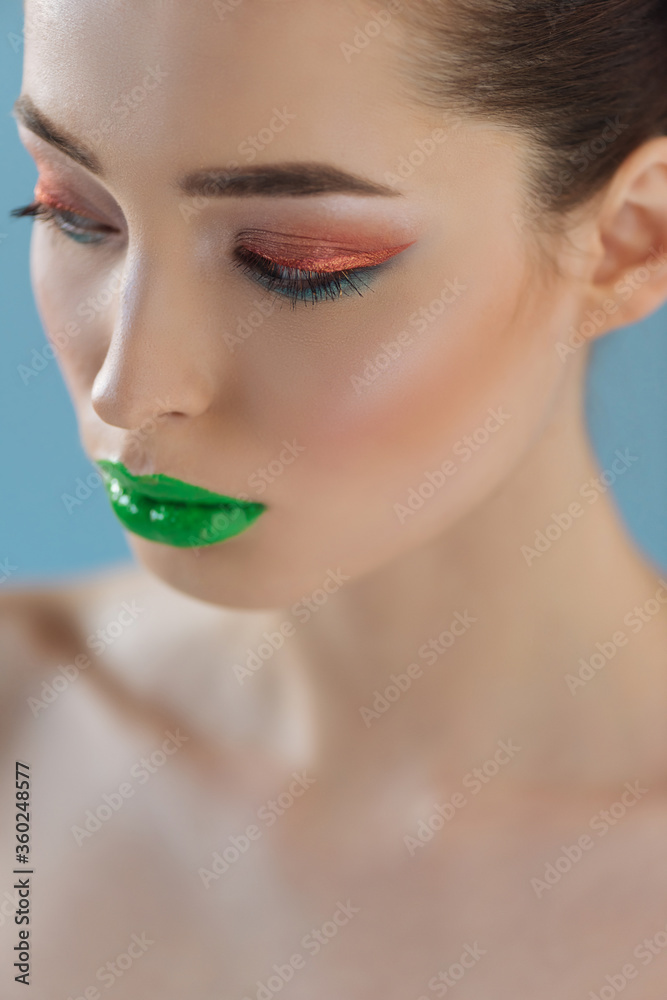 portrait of beautiful naked woman with green lips, pink and blue eyeshadow isolated on blue portrait of beautiful naked woman with green lips, pink and blue eyeshadow isolated on blue