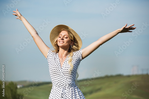 happy woman in a field against the sky. spread your arms. dress and hat copycpase