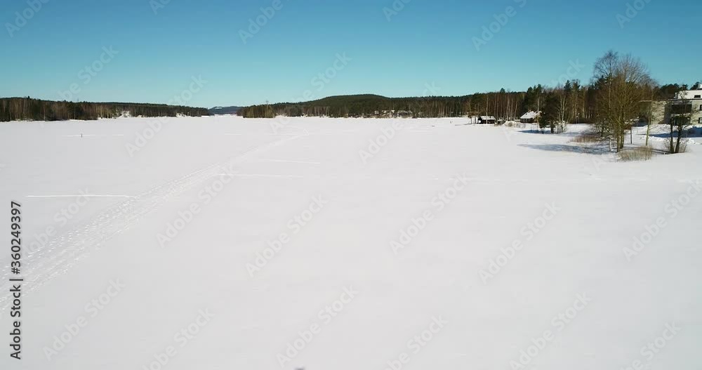Aerial view passing people hiking on snow covered ice, at a arctic lake, on a bright, sunny day, in Kemijarvi, Finland - Dolly, drone shot Aerial view passing people hiking on snow covered ice, at a arctic lake, on a bright, sunny day, in Kemijarvi, Finland - Dolly, drone shot