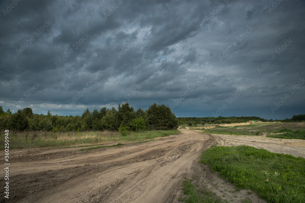 A dirt road in a field before a thunderstorm.