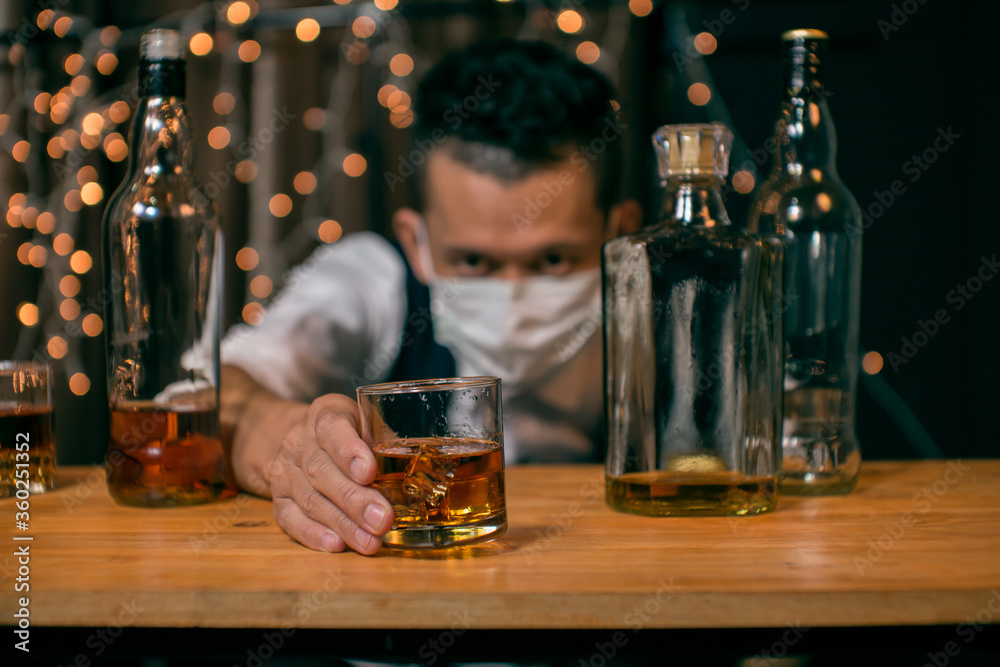 Barman pouring whiskey wearing  protective mask on the bar counter