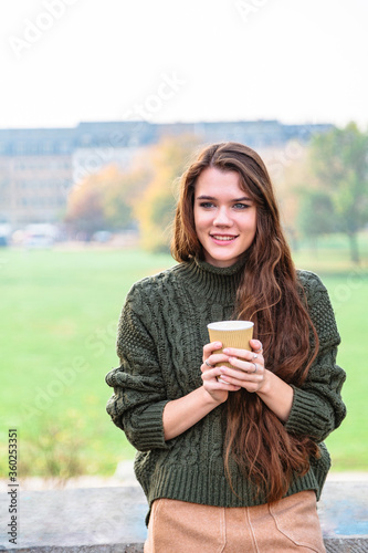 Smiling girl with cup of coffee sits on fence