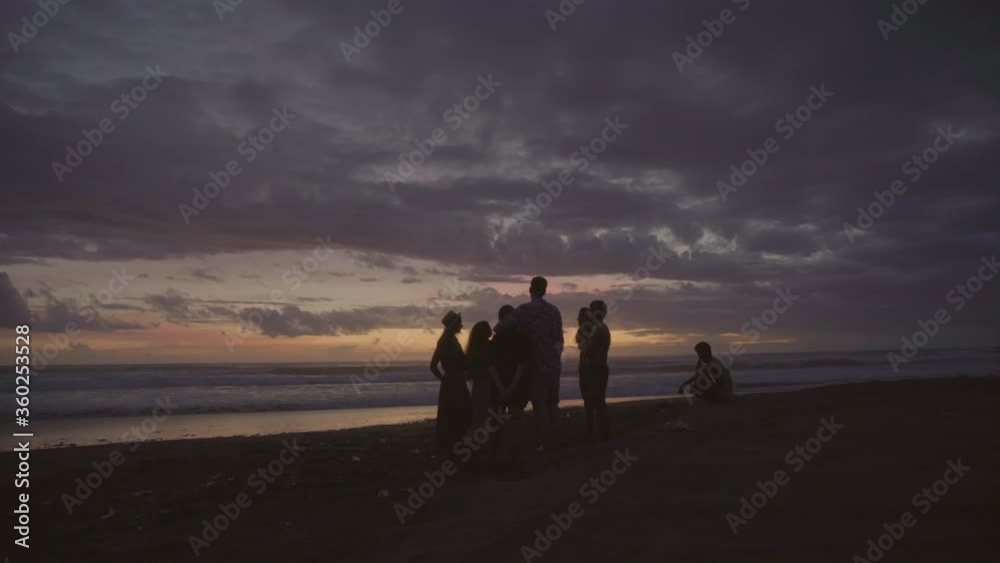 Tracking shot of silhouettes of unrecognizable people standing together on beach on coast of Bali at dusk Tracking shot of silhouettes of unrecognizable people standing together on beach on coast of Bali at dusk